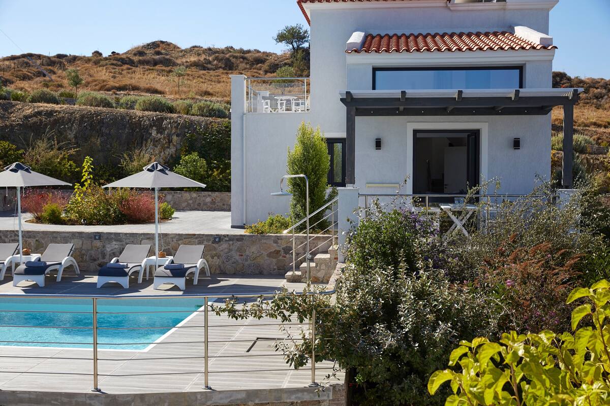 A modern two-story house with a swimming pool, outdoor seating, and a view of the surrounding landscape.