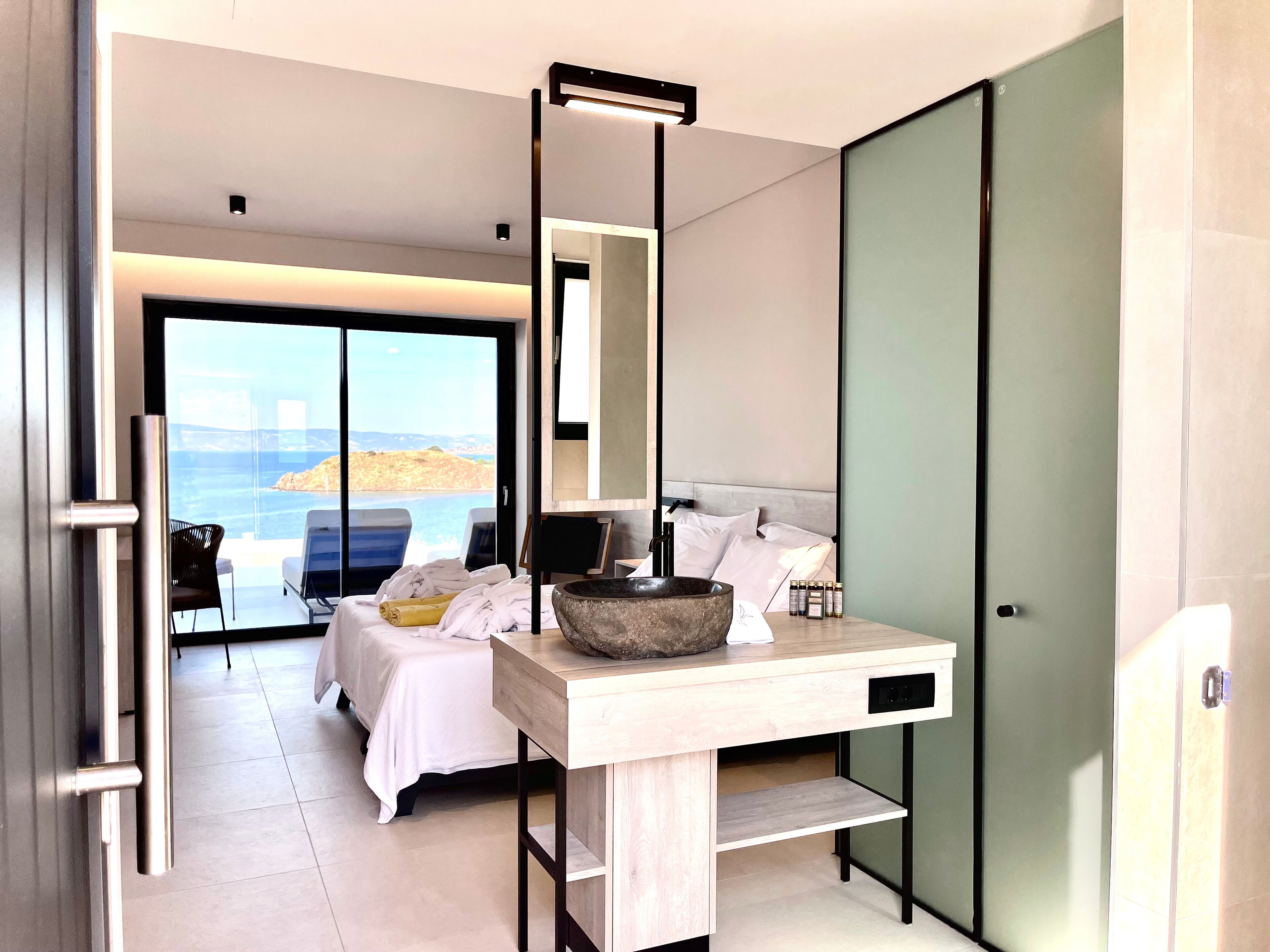 Ein modernes Hotelzimmer mit Bett, einem Holztisch, einer großen Steinschale und Blick auf das Meer.