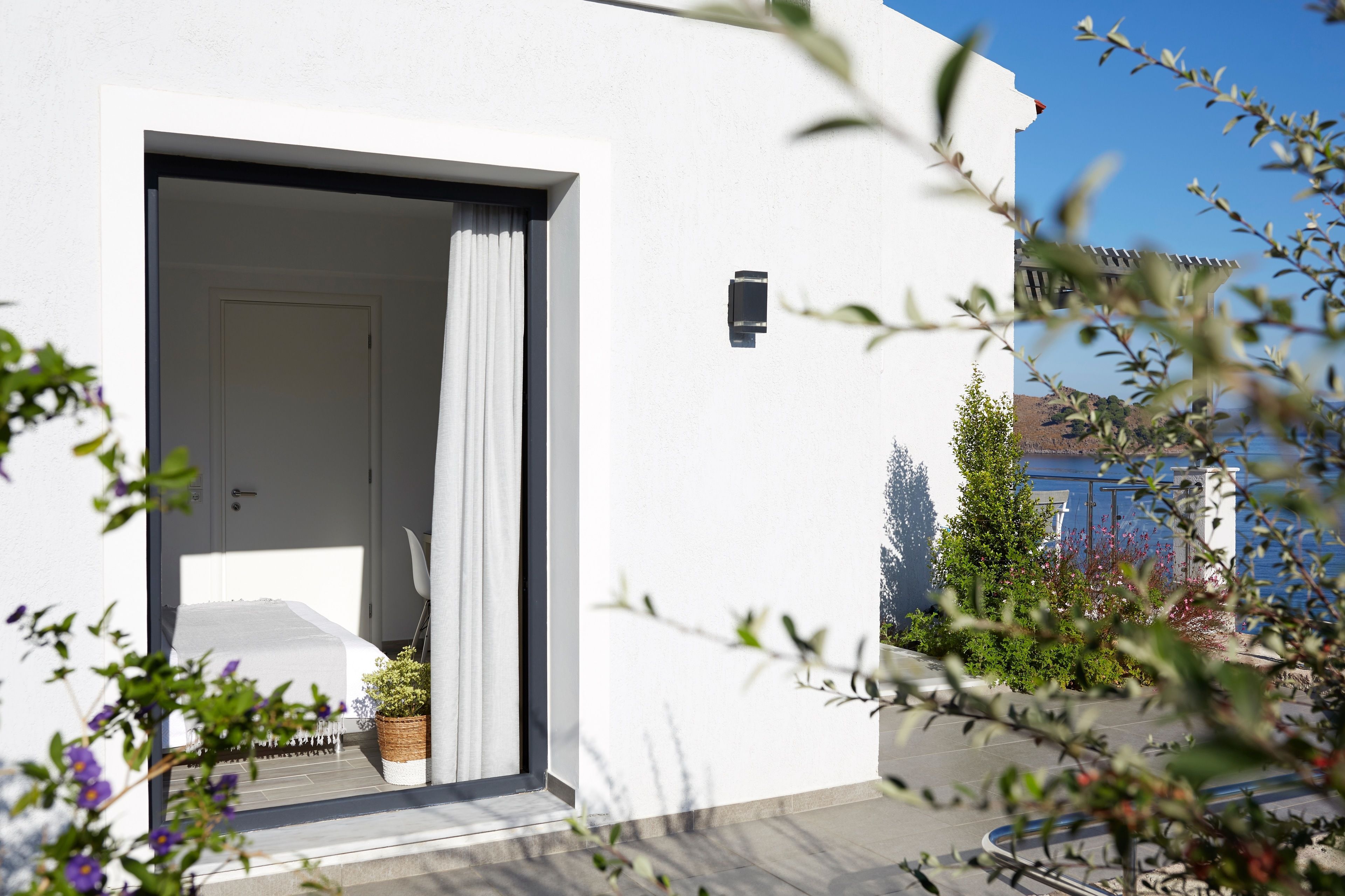 Un bâtiment moderne à la façade blanche, une porte avec un rideau blanc et une petite plante en pot posée sur le sol.