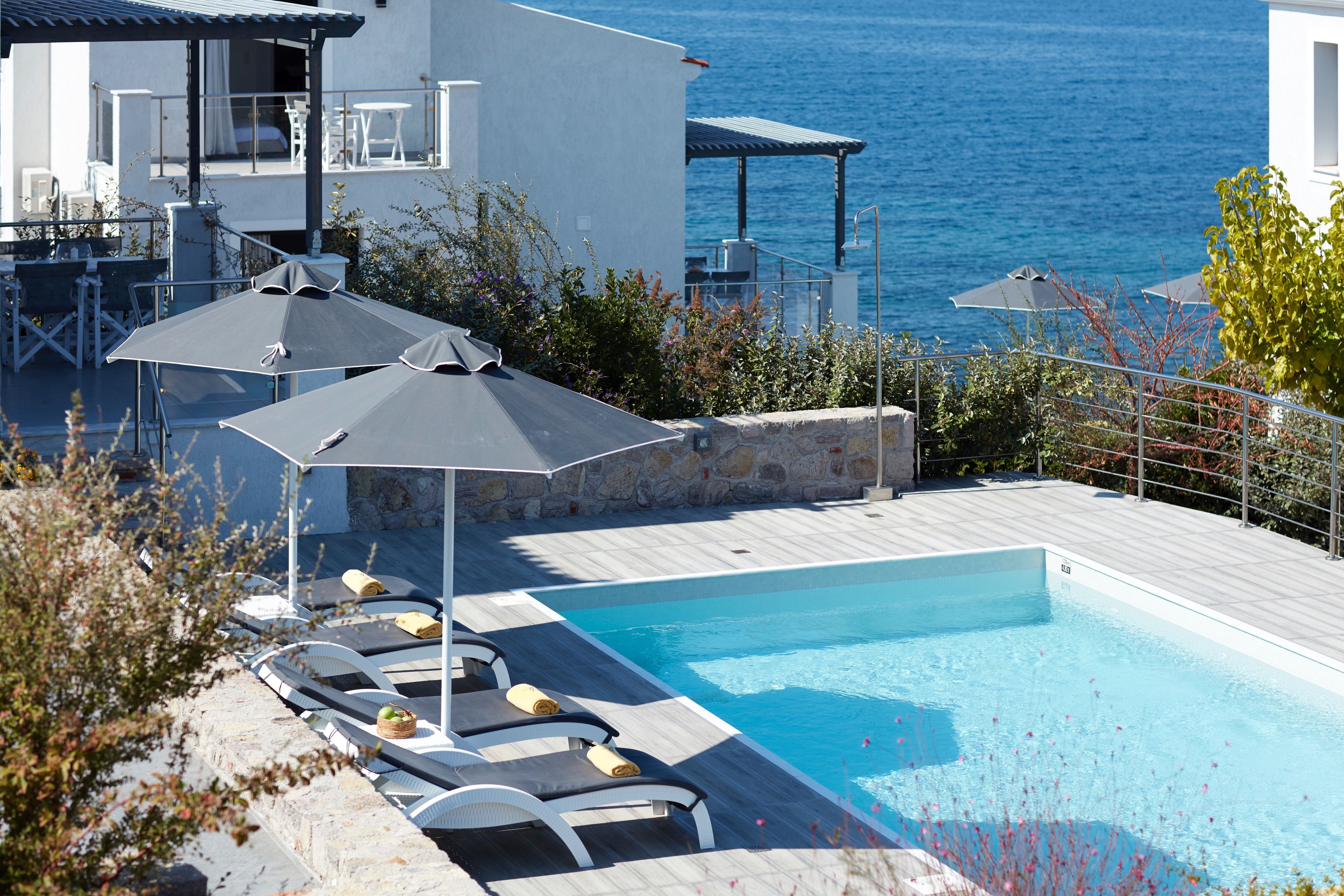 Un espace aménagé au bord de la piscine, avec des chaises longues et des parasols, donnant sur une étendue d’eau.