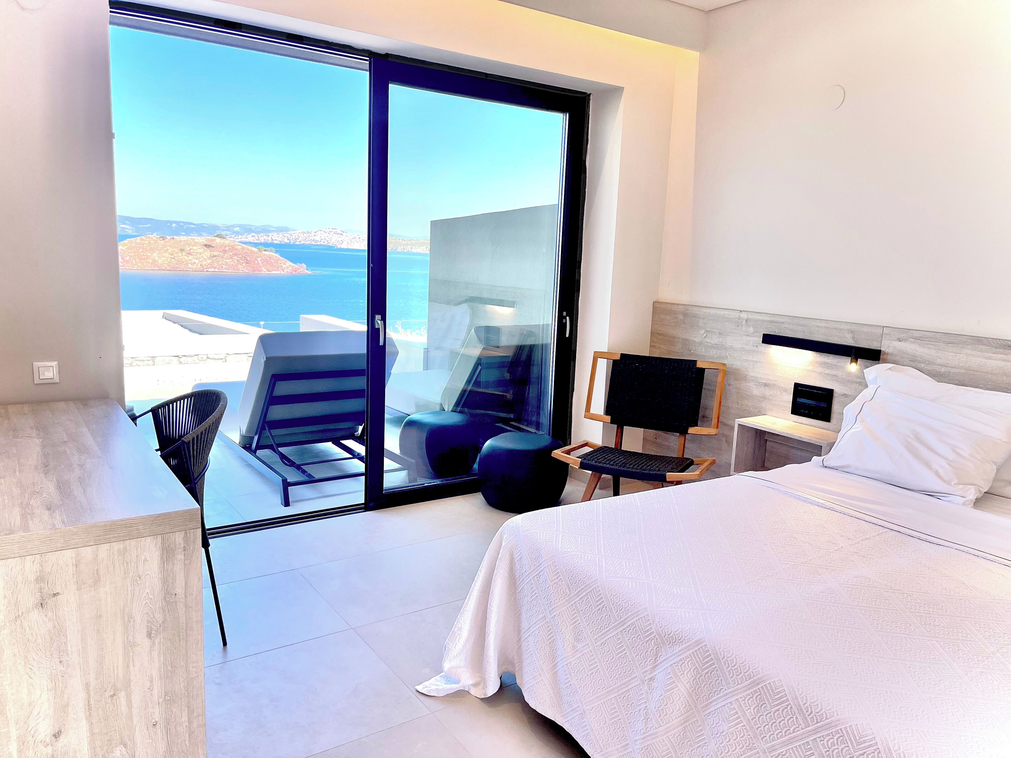 A hotel room with a bed, a desk, a chair, and a view of the sea.