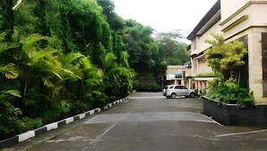 A parking area with a car, surrounded by lush greenery and buildings. - Alam Permai (Bandung)