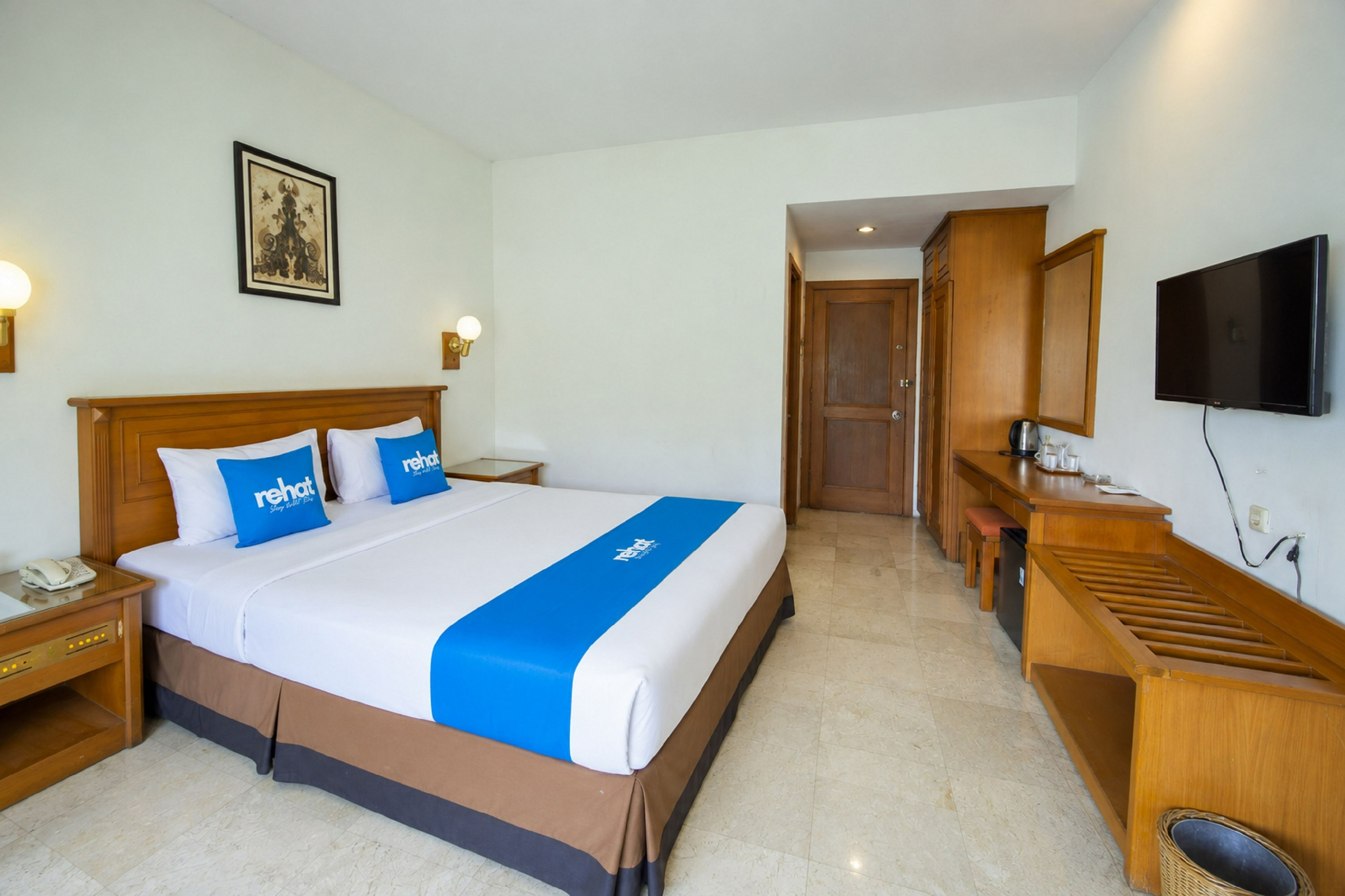 A hotel room with a bed, bedside tables, a desk, a television, and a door leading to another room.