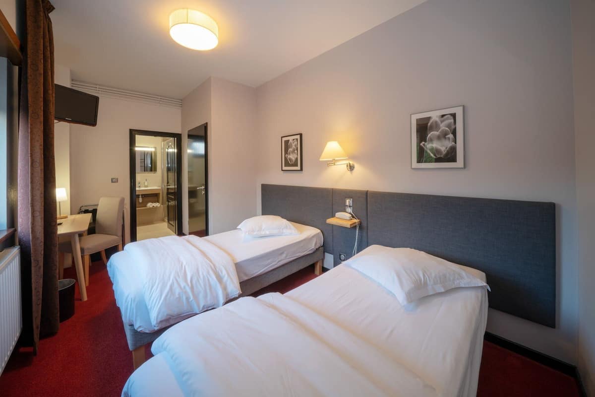 Une chambre d’hôtel avec deux lits, un bureau, une chaise, une salle de bain et un téléviseur.
