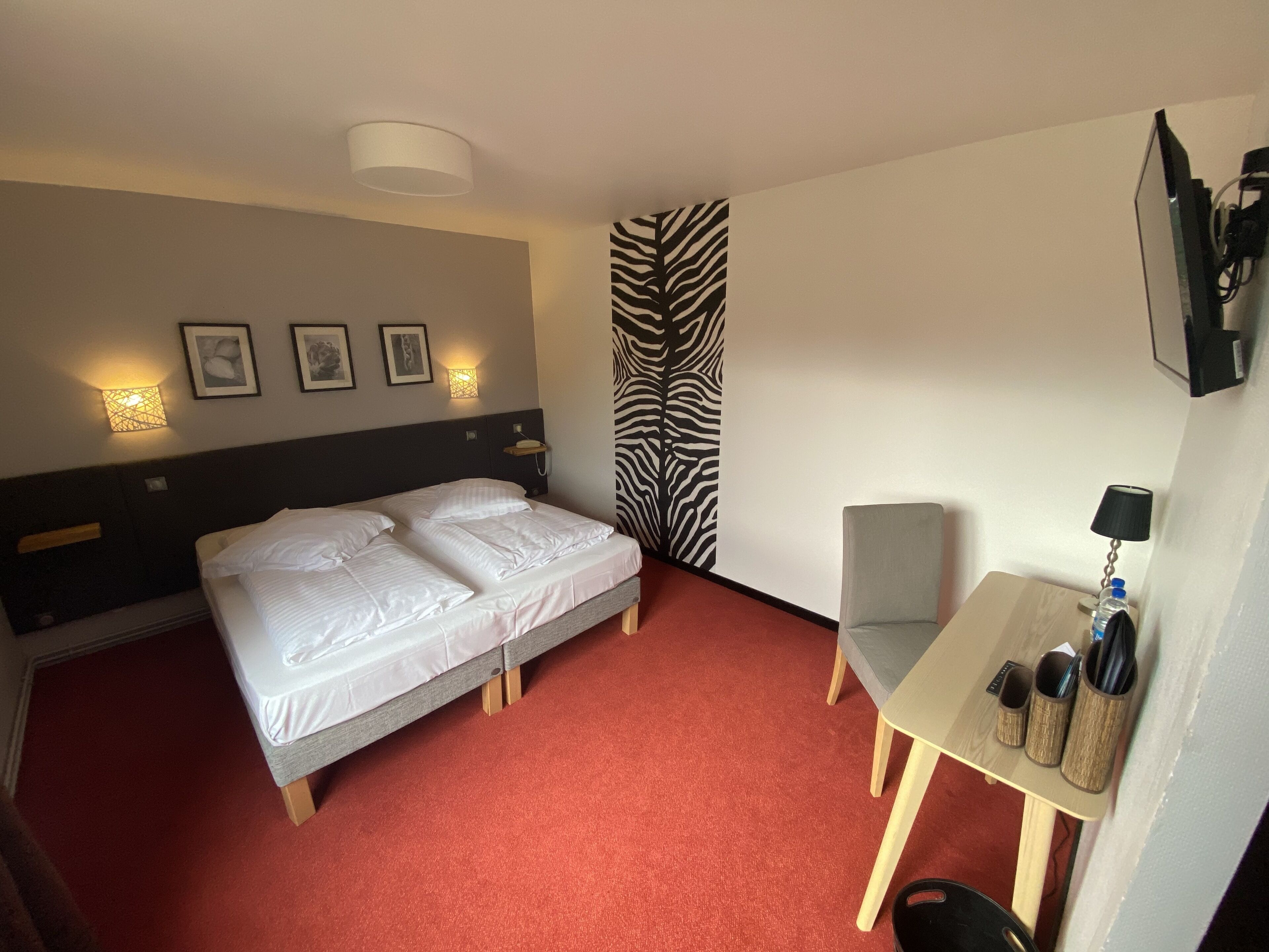 Une chambre d’hôtel avec un lit, un bureau, une chaise, un mur à motifs zébrés et des tableaux encadrés accrochés au mur.