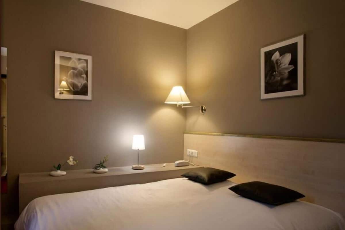 Une chambre d’hôtel avec un lit, une table de chevet, une lampe et deux tableaux encadrés accrochés au mur.