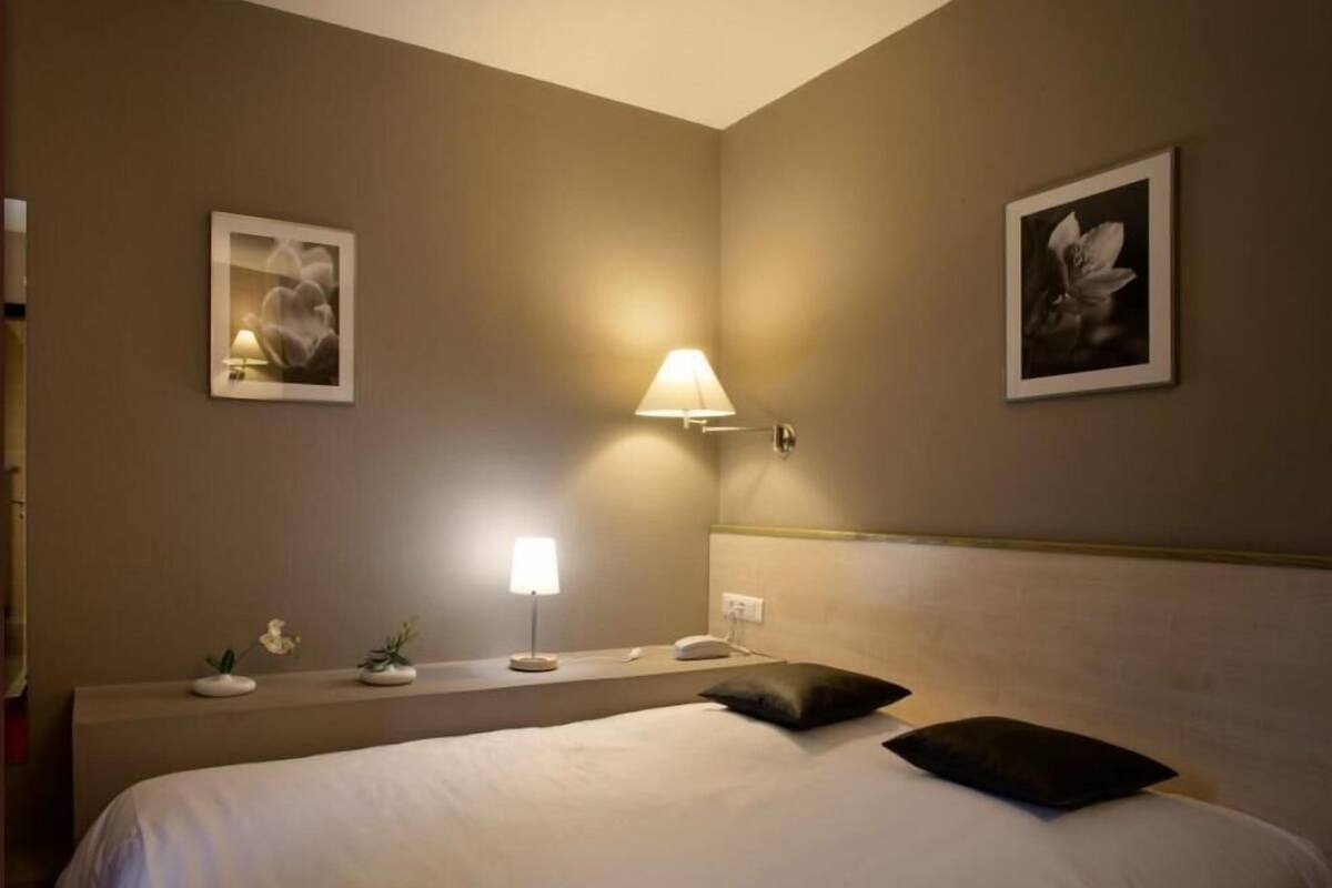 Une chambre d’hôtel avec un lit, une table de chevet, une lampe et deux tableaux encadrés au mur.