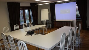 Un salón de conferencias con una larga mesa, sillas blancas, una pantalla de proyector y una pizarra.