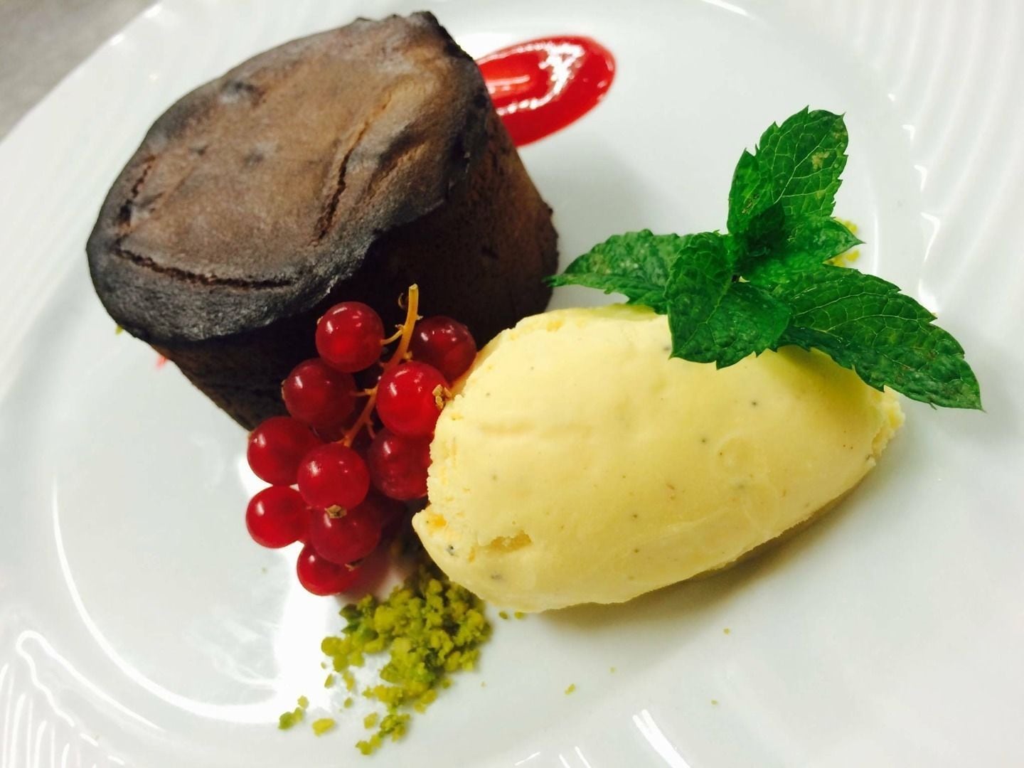 Ein Dessertteller mit Schokoladenkuchen, roten Johannisbeeren, einer Kugel Vanilleeis und einem Minzblatt als Garnitur.