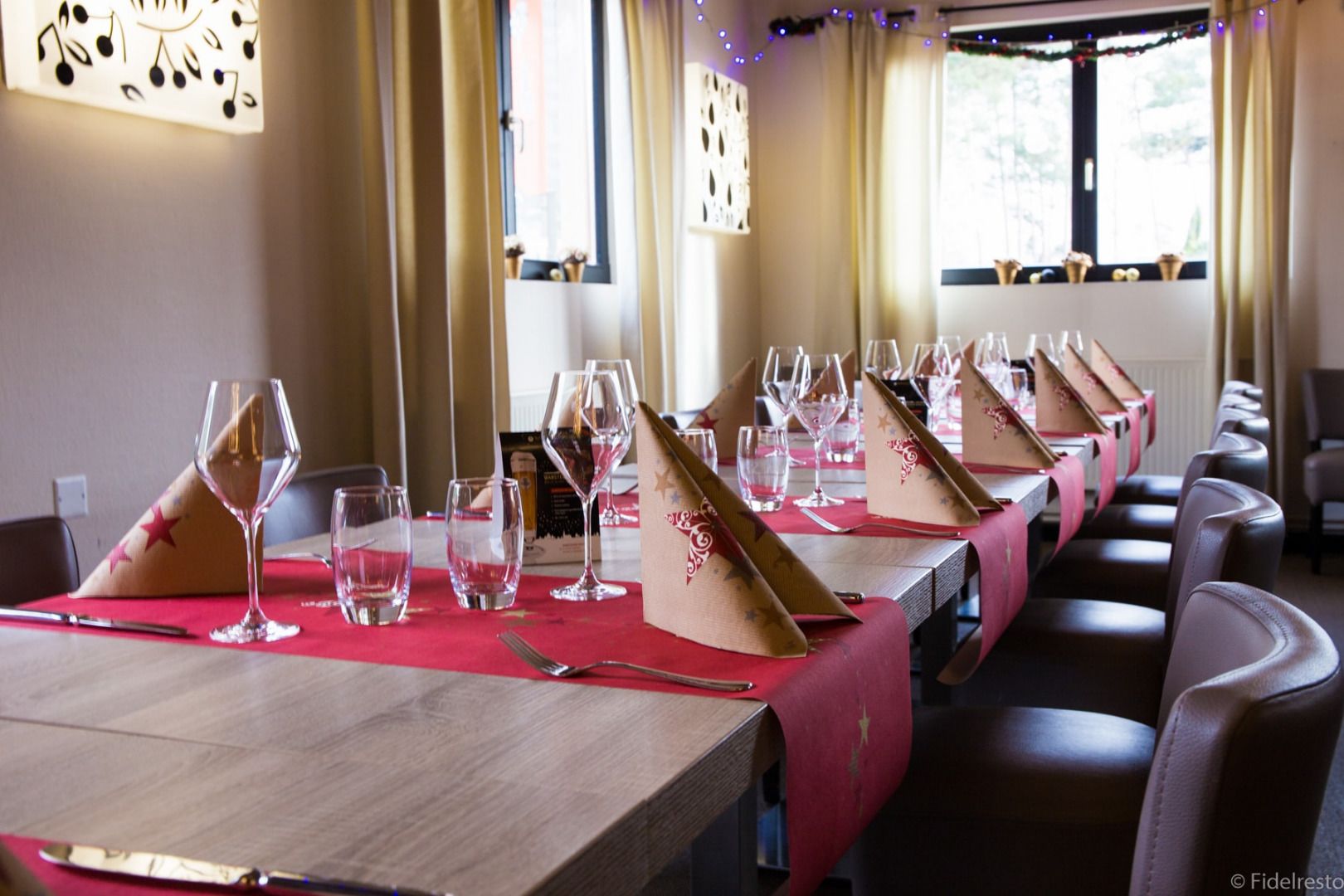 A long dining table with multiple wine glasses and napkins, set in a room with large windows and curtains.