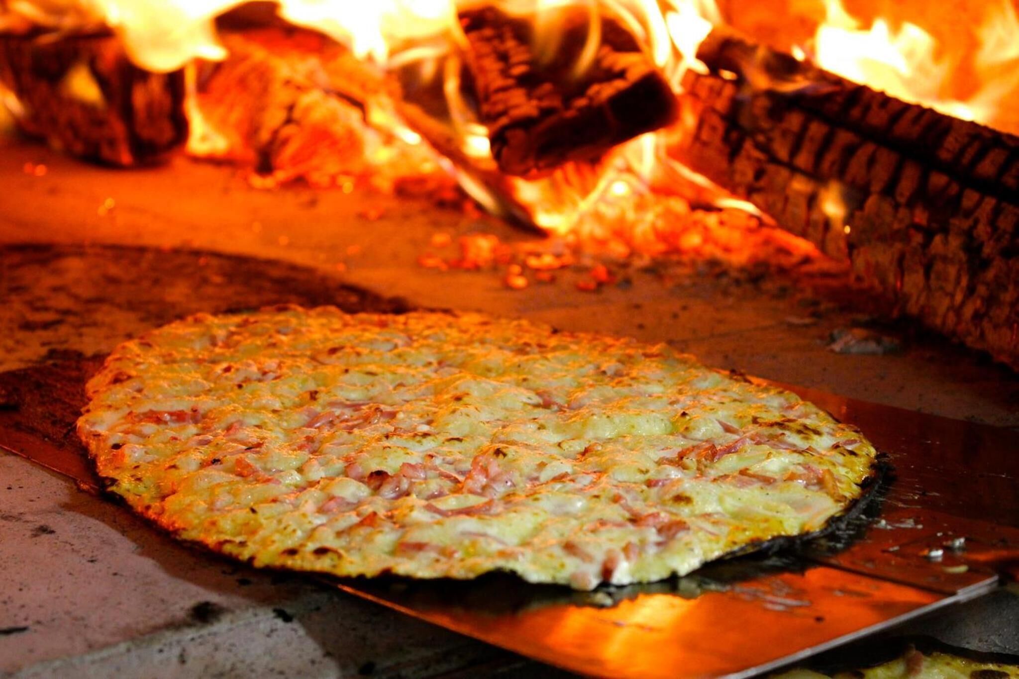Pizza sendo assada em forno a lenha.