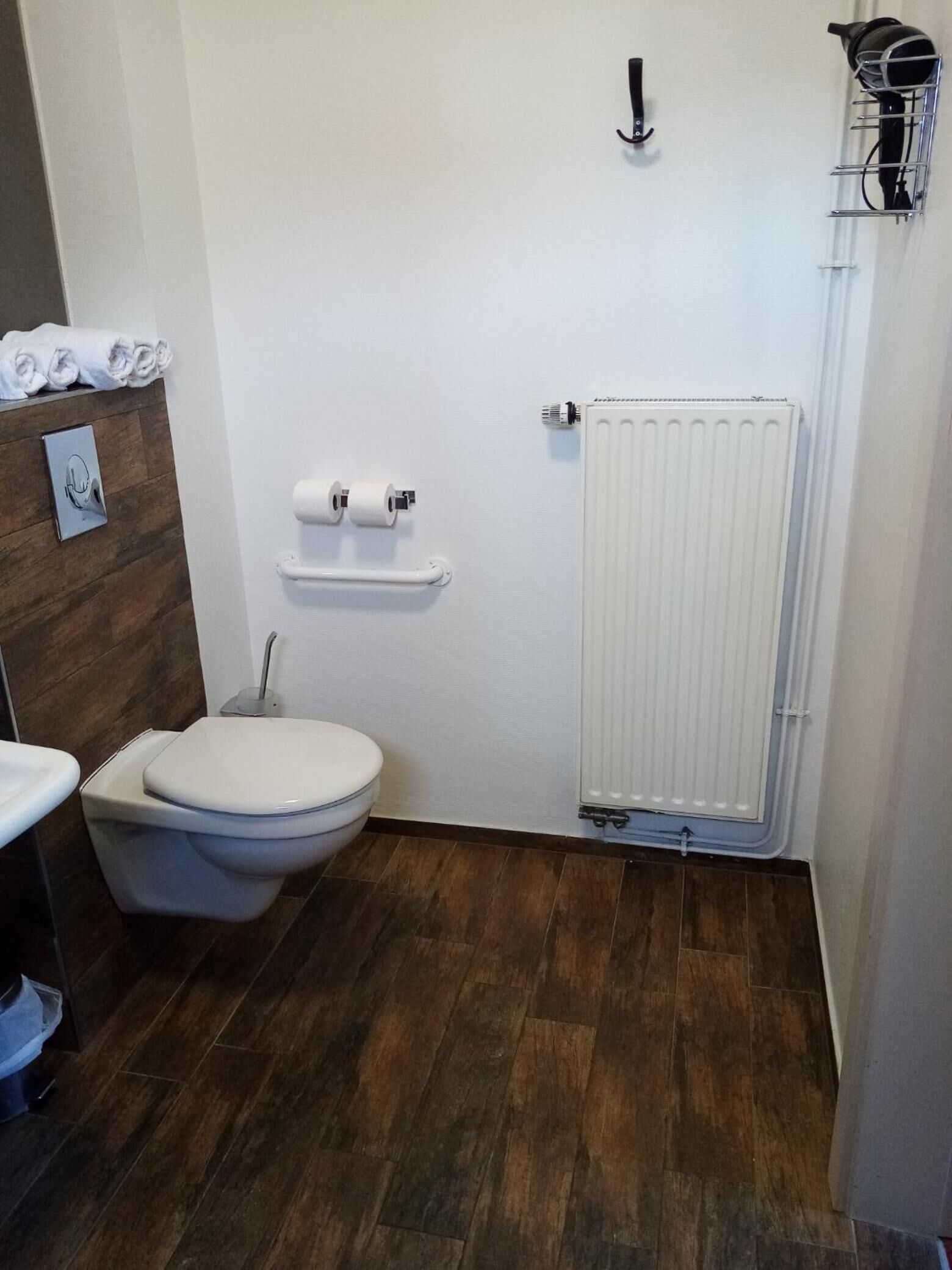 Ein kleines, modernes Badezimmer mit Toilette, Waschbecken und Handtuchwärmer – alles in Weiß.