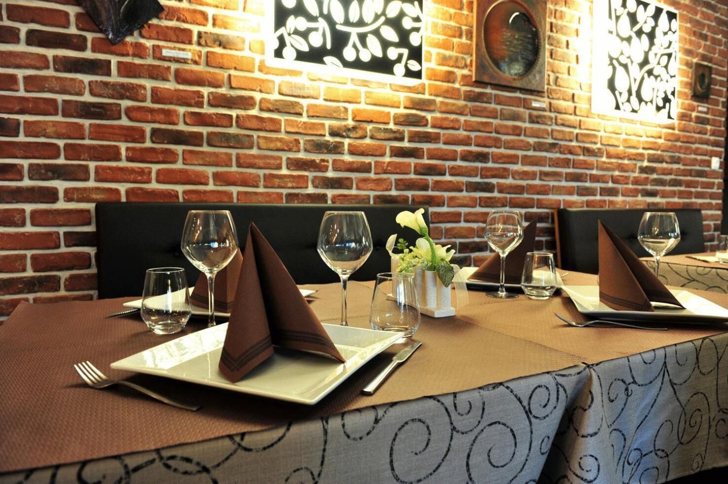 A restaurant with brick walls and a table set for four with wine glasses, plates, and napkins.