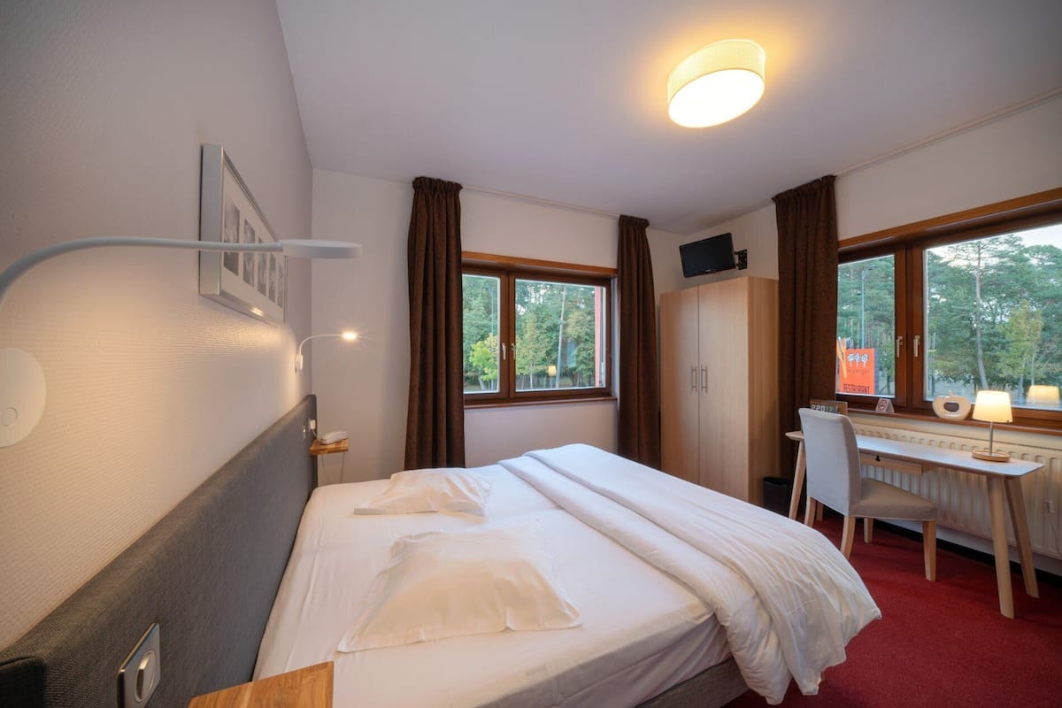Une chambre d’hôtel équipée d’un lit, d’un bureau, d’une chaise et d’une fenêtre donnant sur la forêt.