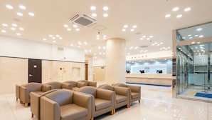 A modern lobby with beige sofas arranged in a semi-circle, a reception desk, and a glass partition wall.