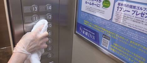 A hand using a tissue to clean an elevator button panel.