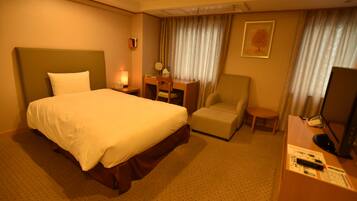 A hotel room with a large bed, a desk with a chair, a television, and a small table.