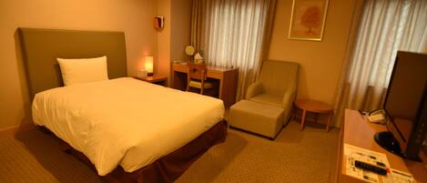 A hotel room with a large bed, a desk with a chair, a television, and a small table.
