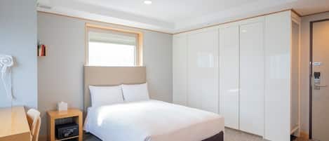 Ein Hotelzimmer mit Bett, Nachttisch, Lampe, Kleiderschrank und Fenster.
