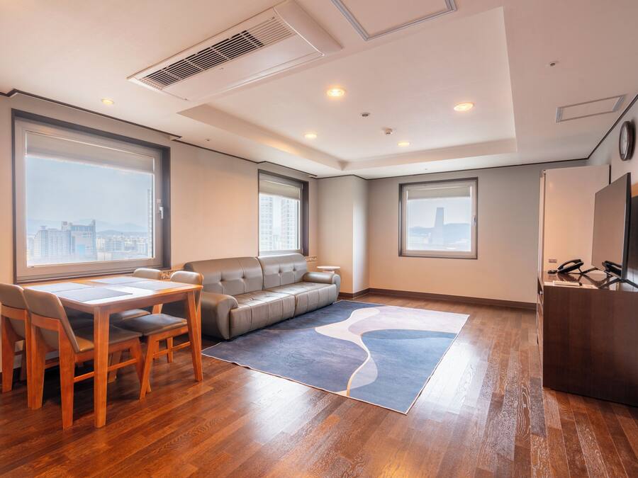 Una habitación de hotel moderna con mesa de comedor, sofá y grandes ventanales con vistas a la ciudad.