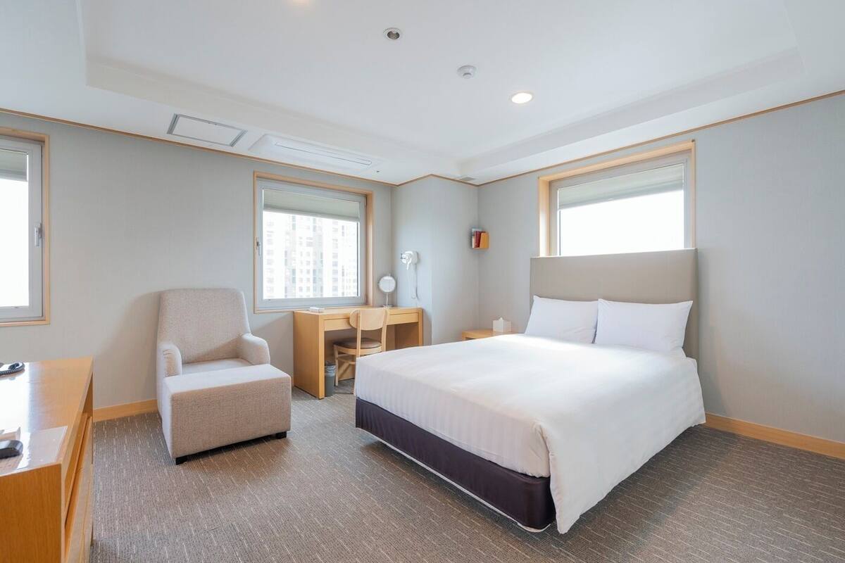A hotel room with a bed, a desk, a chair, and a window.