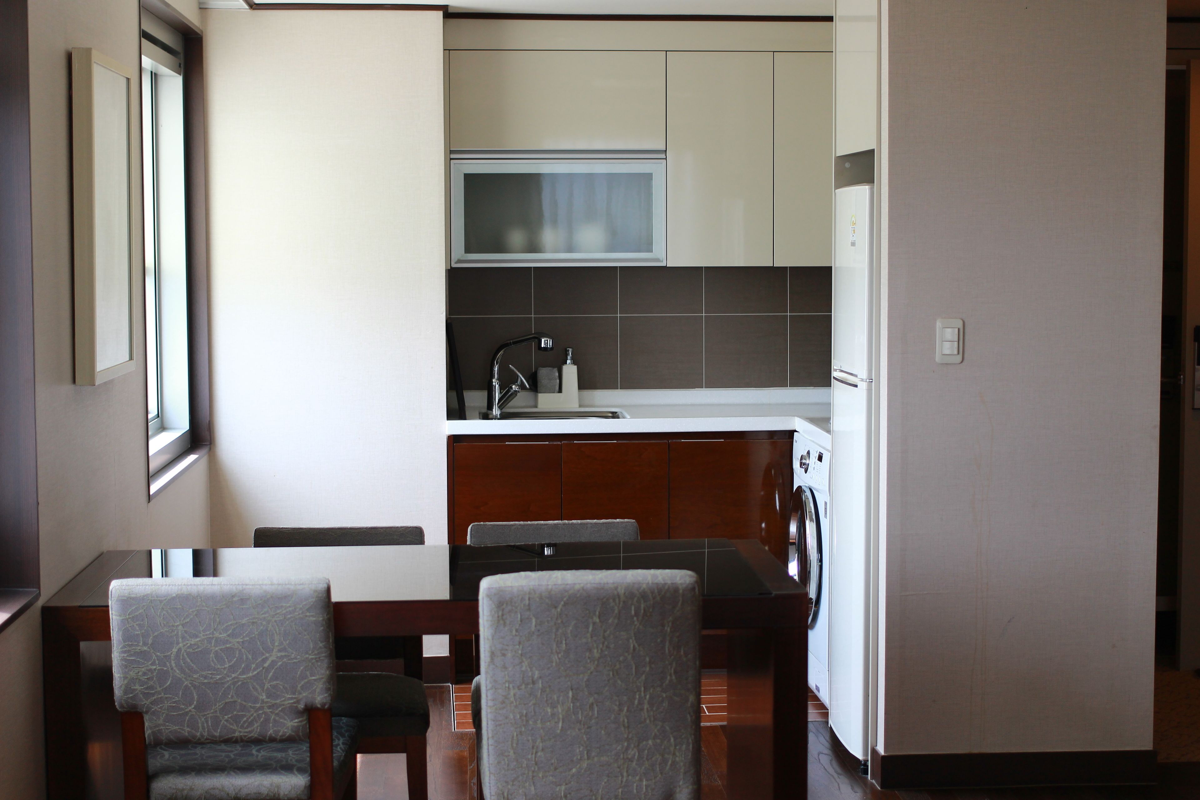 Cocina compacta con microondas, pileta y lavadora. En el comedor, hay dos sillas y una mesa.