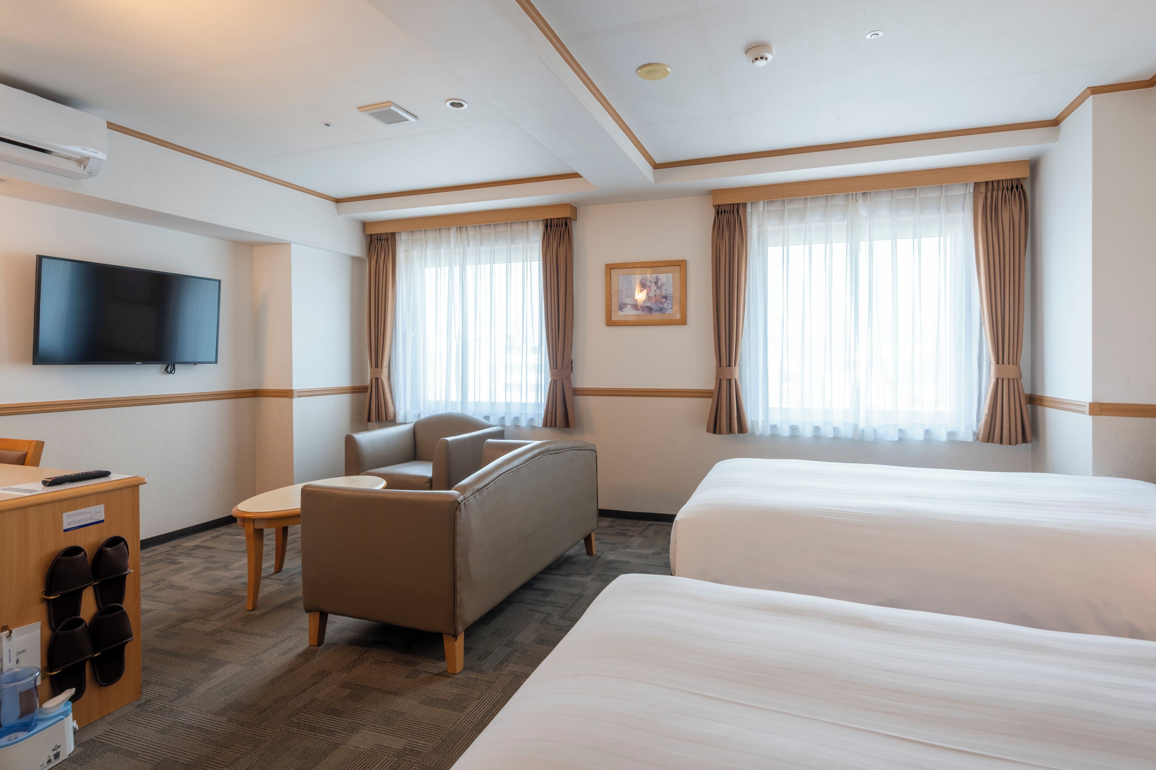 A hotel room with a flat-screen TV, a sofa, a small table, and two beds.