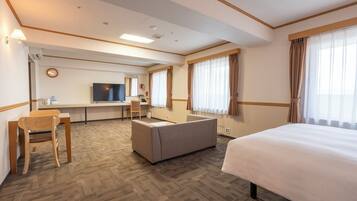 A hotel room with a bed, a desk, a television, and a seating area.