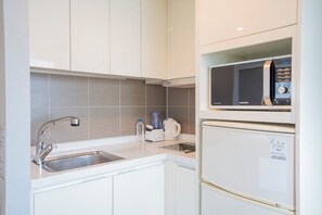 A modern kitchen with white cabinetry, a stainless steel sink, a microwave, and a refrigerator.