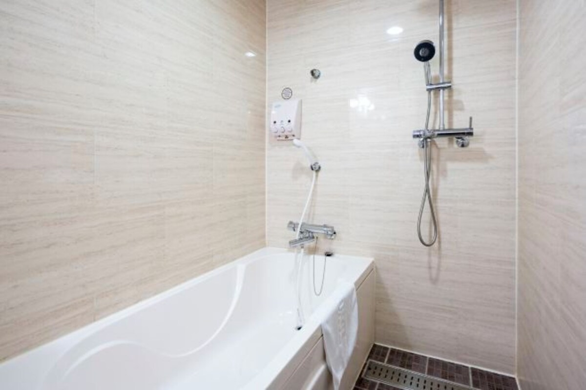 A modern bathroom with a white bathtub, a shower with a handheld showerhead, and a wall-mounted control panel.