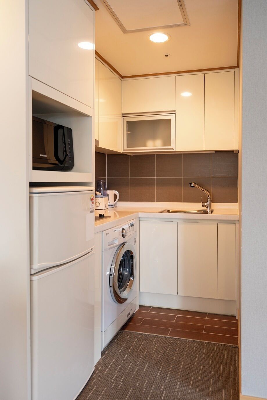 A compact kitchen with a microwave, washing machine, sink, and cabinets.