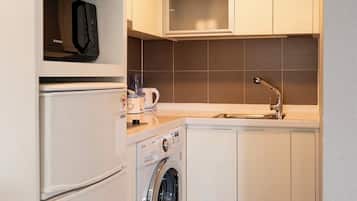 A compact kitchen with a microwave, washing machine, sink, and cabinets.
