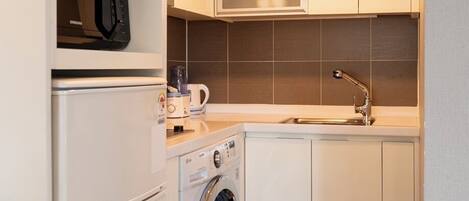 A compact kitchen with a microwave, washing machine, sink, and cabinets.