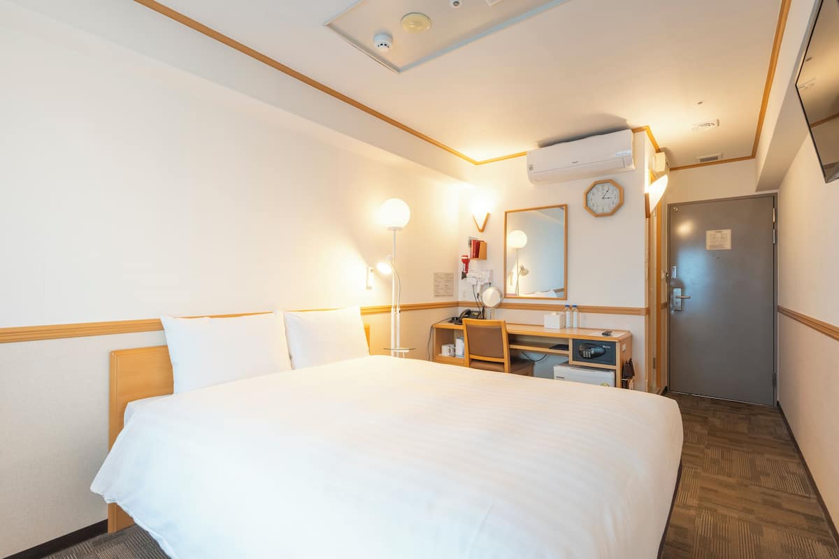A hotel room with a large bed, a desk with a chair, a mirror, and a clock on the wall.