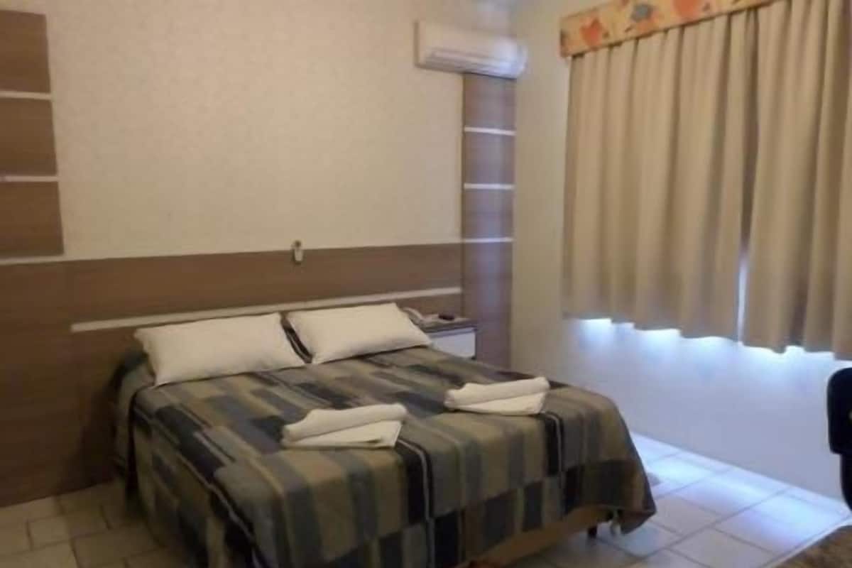 A hotel room with a bed, a nightstand, and a window with curtains.