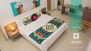 A hotel room with a bed, a desk, and a chair. The room has a painting on the wall and a window. - Hotel Unión Plaza Moteria (Monteria)