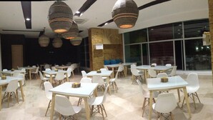 A spacious dining area with multiple tables and chairs, large windows, and hanging pendant lights. - Hotel Unión Plaza Moteria (Monteria)