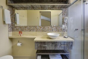 A bathroom with a stone mosaic backsplash, a large mirror, a white sink, and a shower area. - Pietra Flat (Florianópolis)