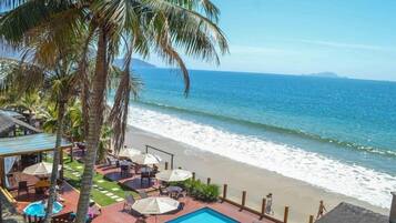 Un hotel frente a la playa con piscina, sombrillas y palmeras.