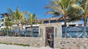 A modern hotel with a stone facade, palm trees, and a clear blue sky. - Pietra Flat (Florianópolis)