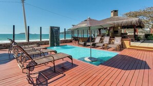 A wooden deck with a pool, lounge chairs, and umbrellas. - Pietra Flat (Florianópolis)