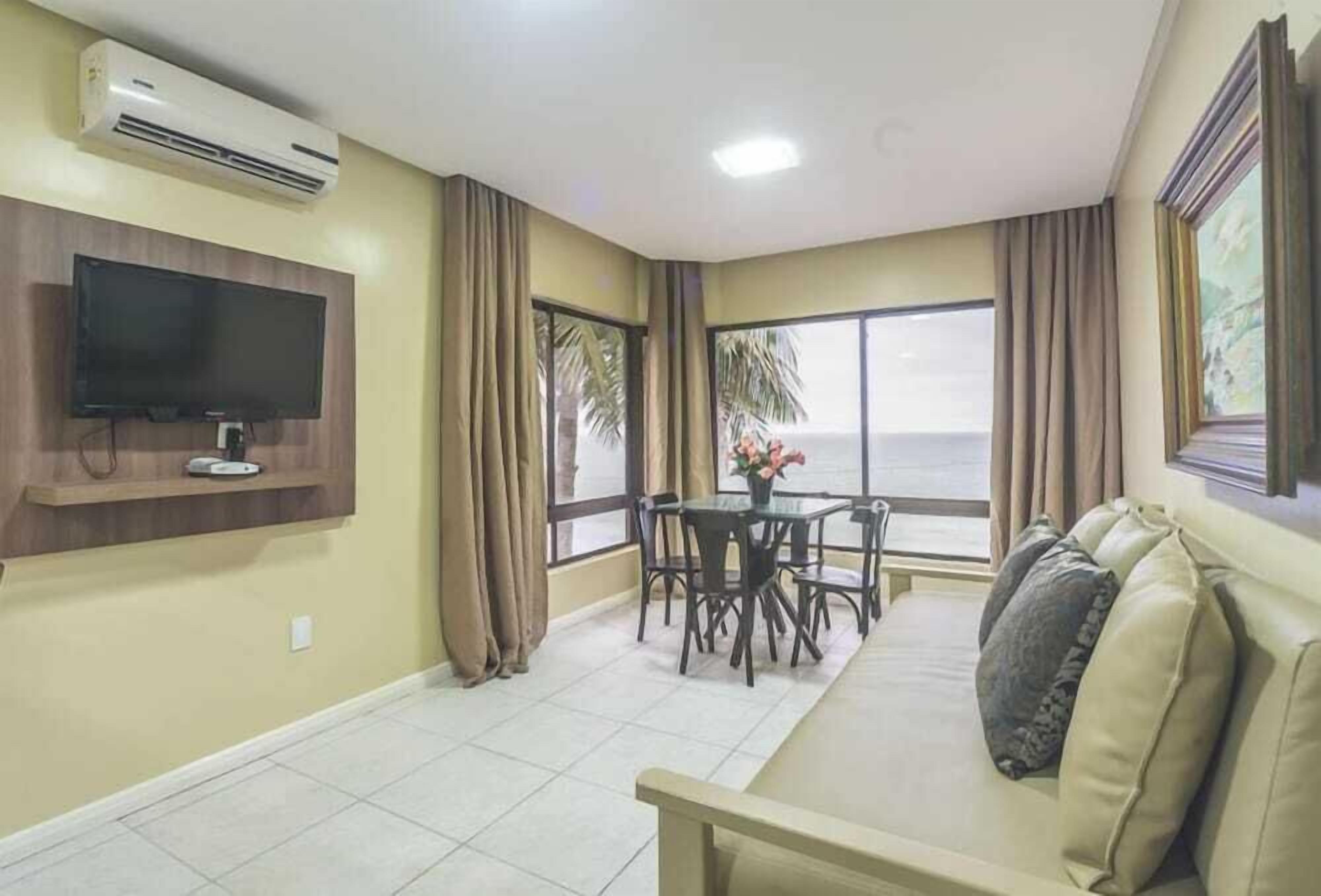 Una sala de estar con televisor, sofá, mesa de comedor y sillas, y vista al mar.