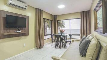 Una sala de estar con televisor, sofá, mesa de comedor y sillas, y vista al mar.