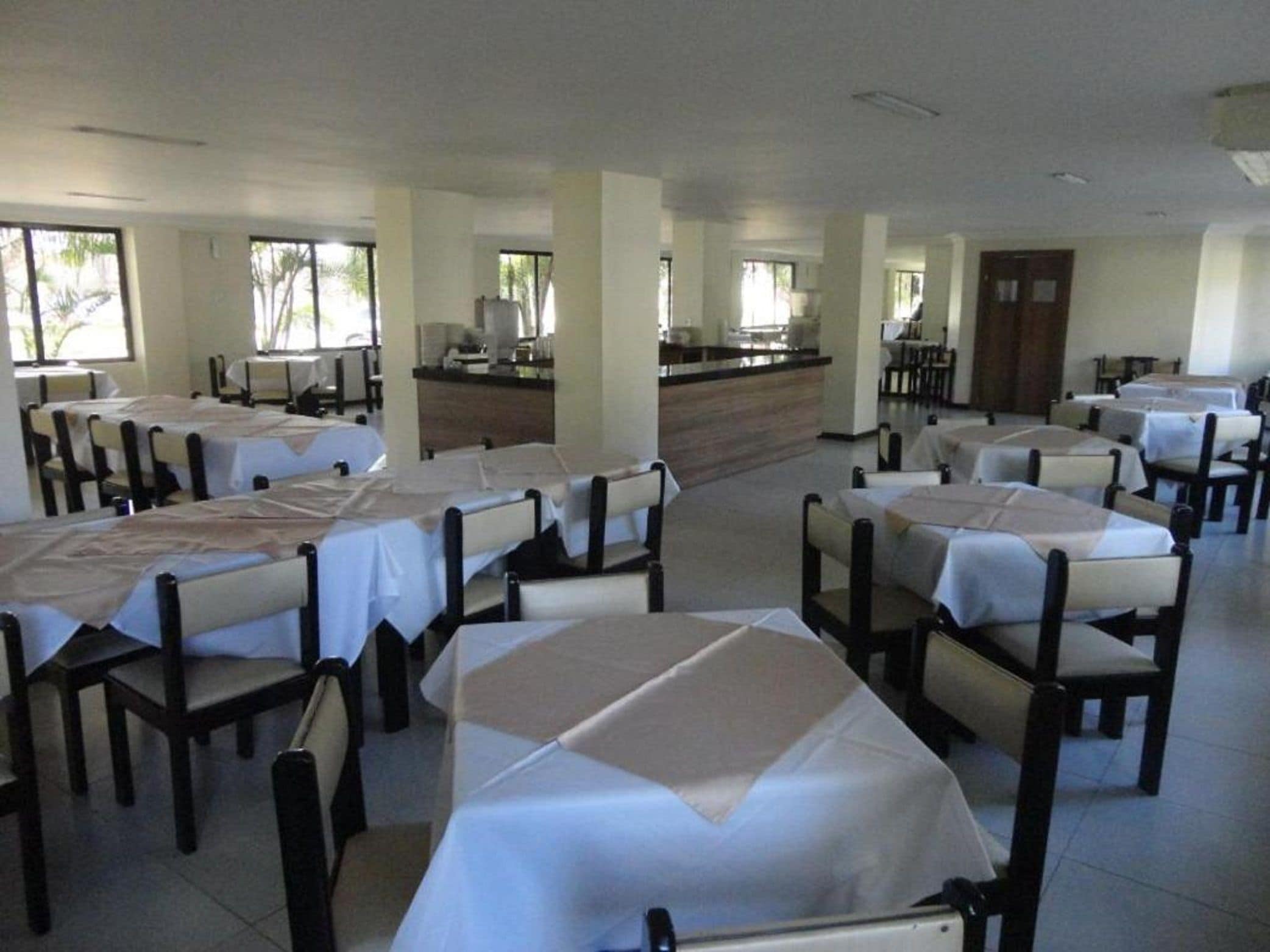 A spacious dining area with multiple tables and chairs, a central counter, and large windows allowing natural light.