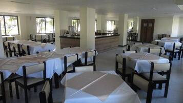 A spacious dining area with multiple tables and chairs, a central counter, and large windows allowing natural light.