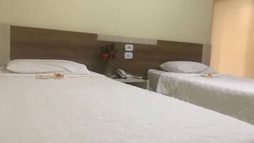A hotel room with two single beds, a wooden headboard, a bedside table with a phone, and a vase with flowers.