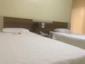 Een hotelkamer met twee eenpersoonsbedden, een houten hoofdbord, een nachtkastje met telefoon en een vaas met bloemen.