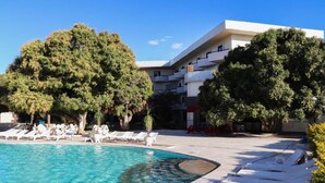 A swimming pool with lounge chairs, surrounded by trees and a building with balconies.