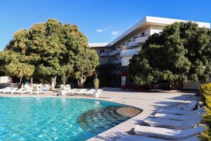 Una piscina con sillas de descanso, rodeada de árboles y un edificio con balcones.