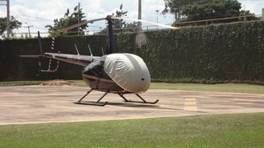 A stationary helicopter on a concrete surface with a grassy area and a hedge in the background.
